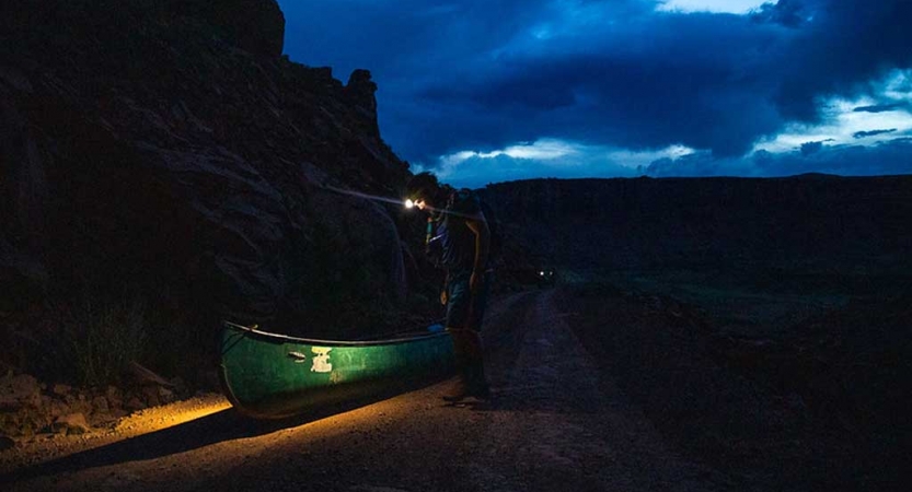 a student wearing a headlamp illuminates a canoe on an outward bound expedition 